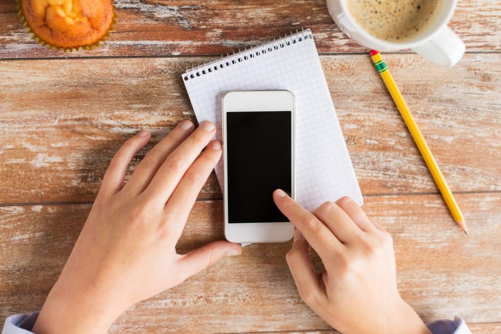 business, education, people and technology concept - close up of male hands with smartphone, notebook and pencil on wooden table